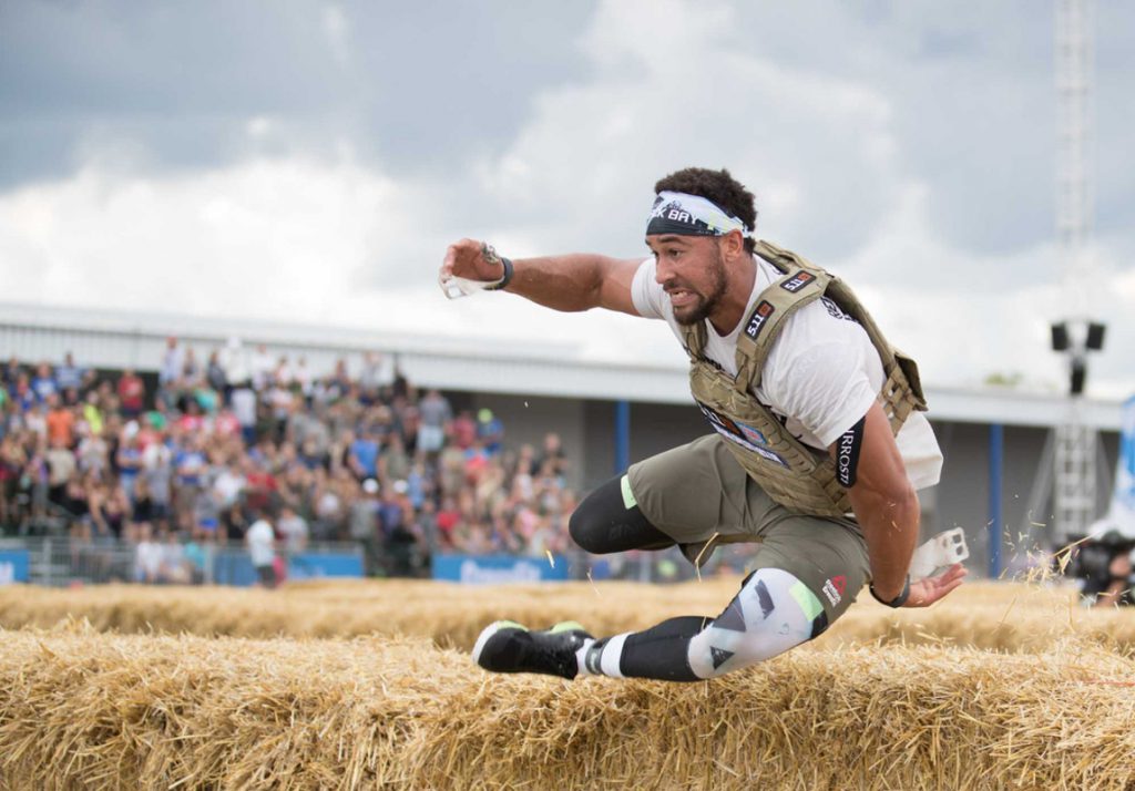 Male Crossfit Athlete with weight vest leaps over a hay bail at the crossfitgames in Madison, Wisconsin