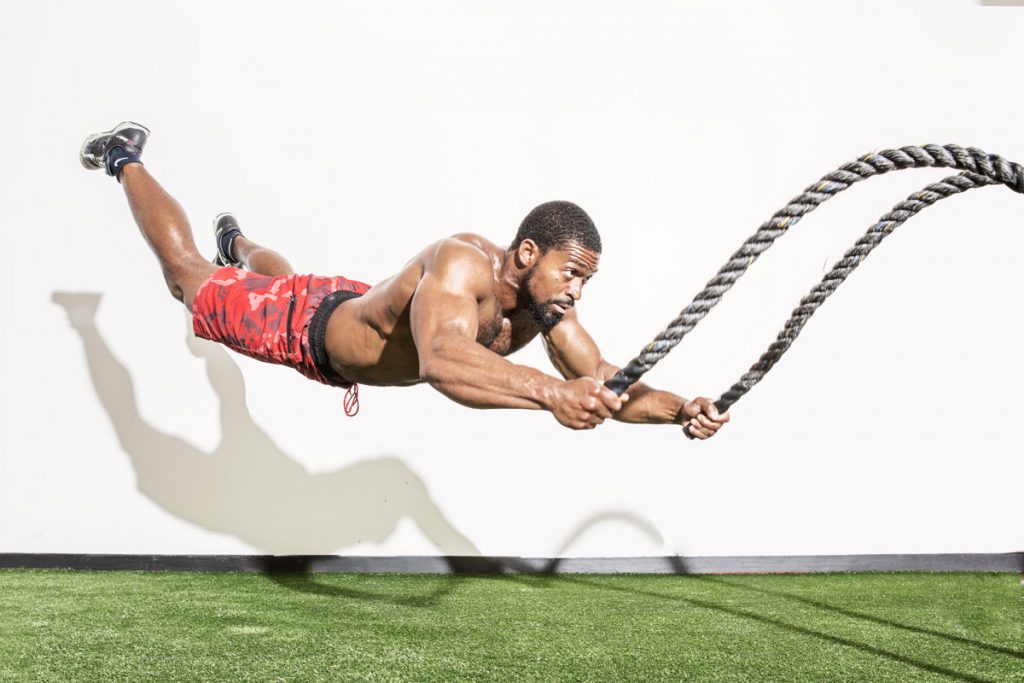 male athlete, Andre Crews leaps in the air with battle ropes for an athletic photoshoot showing off his muscles and athletic strength and skill